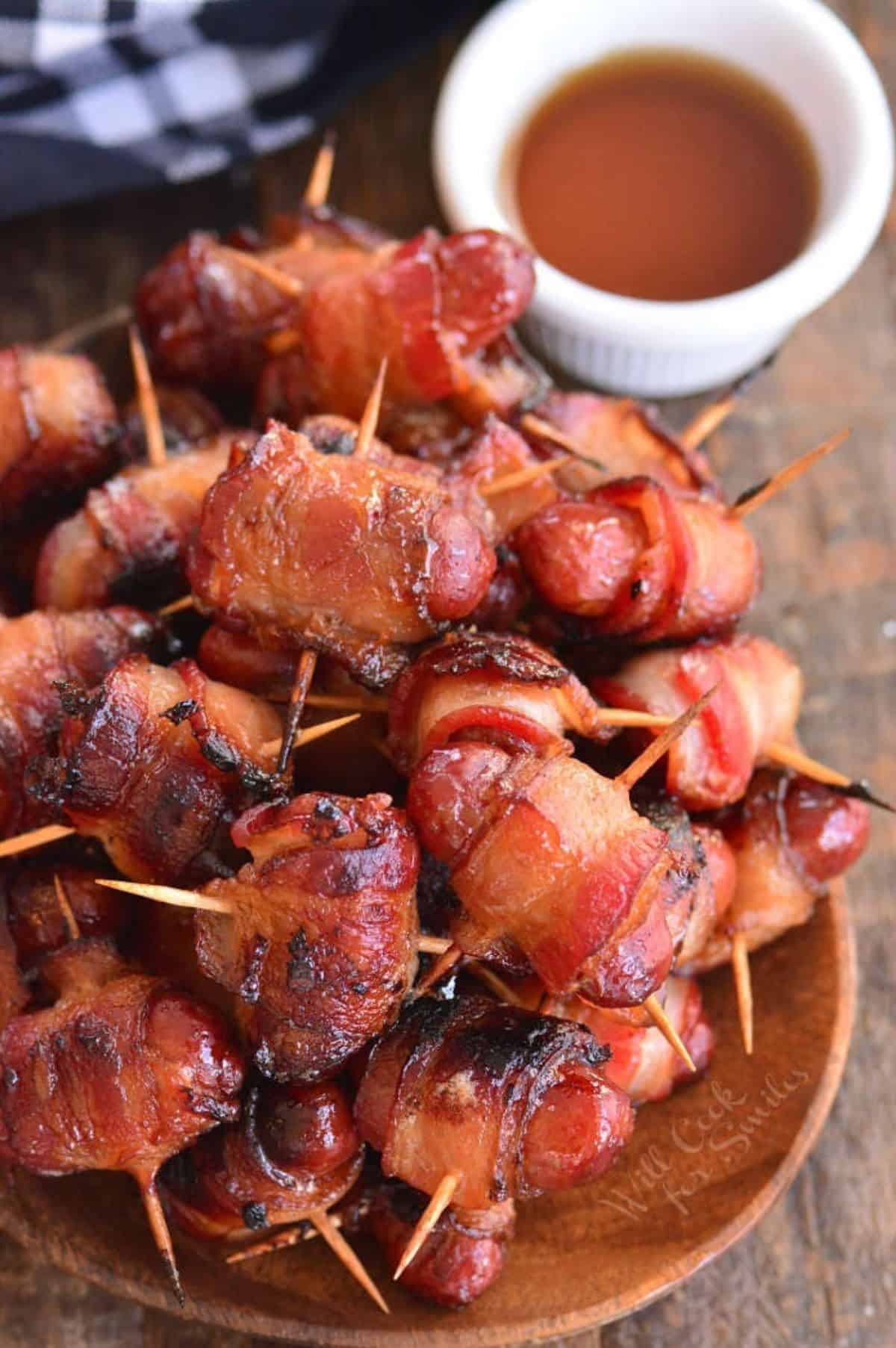 several little smokies sausages wrapped in bacon next to some maple syrup.