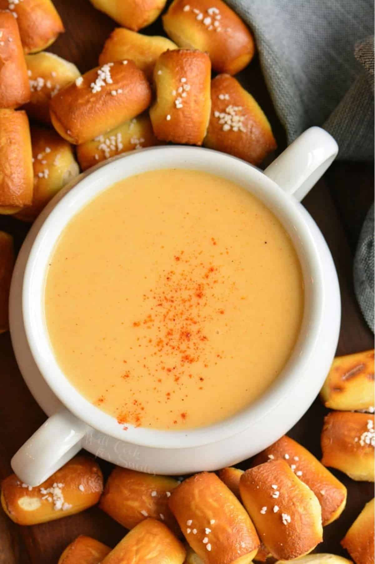 beer cheese dip in a white pot with small pretzel bites around and a blue towel.