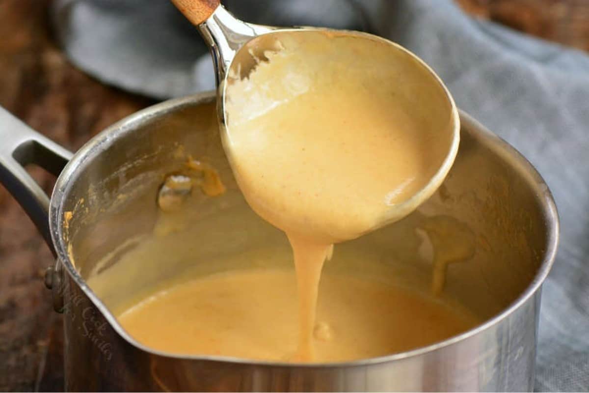 scooping some beer cheese dip from a pot with a ladle.