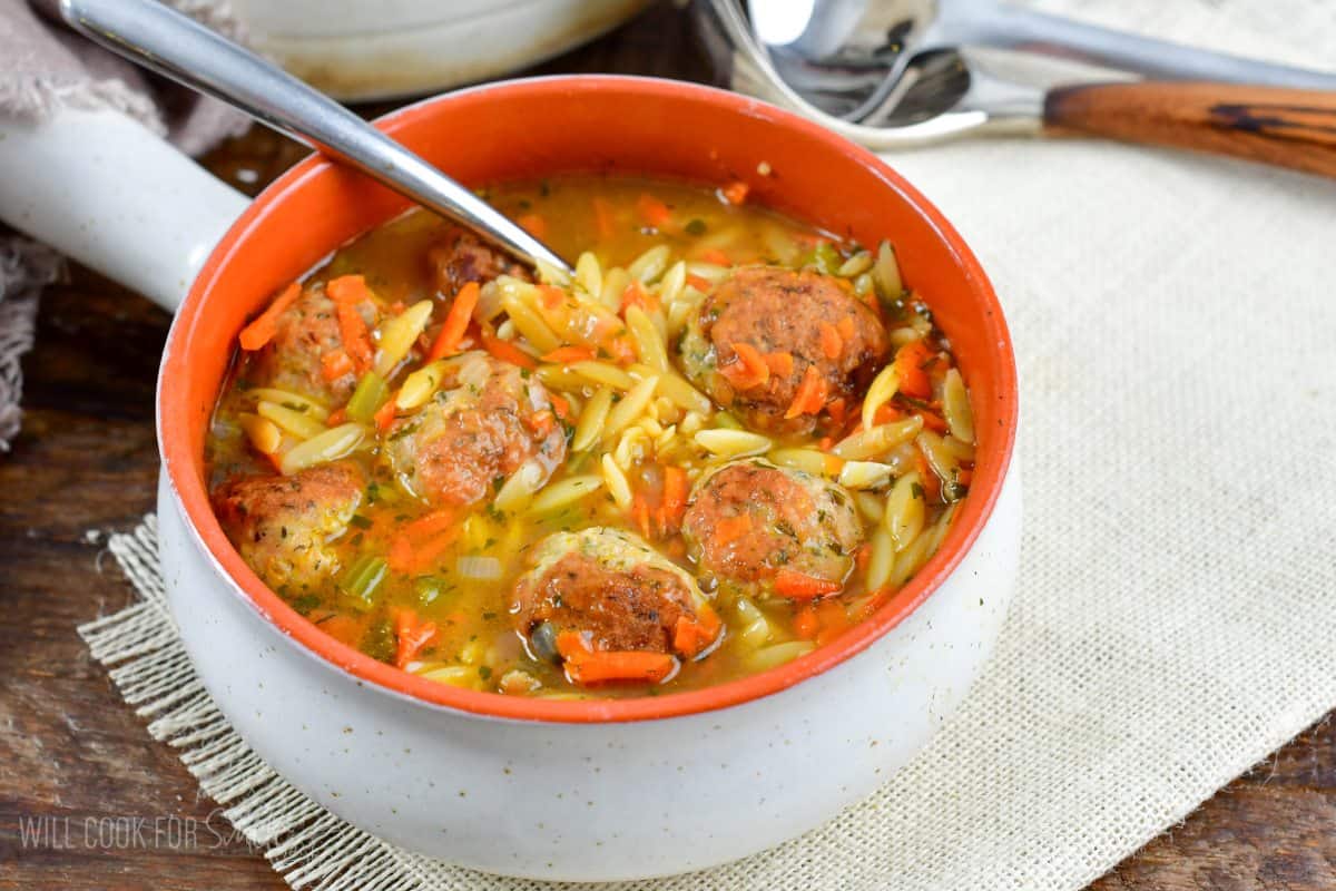 Chicken Meatball and orzo soup in a bowl with a spoon on a placemat.