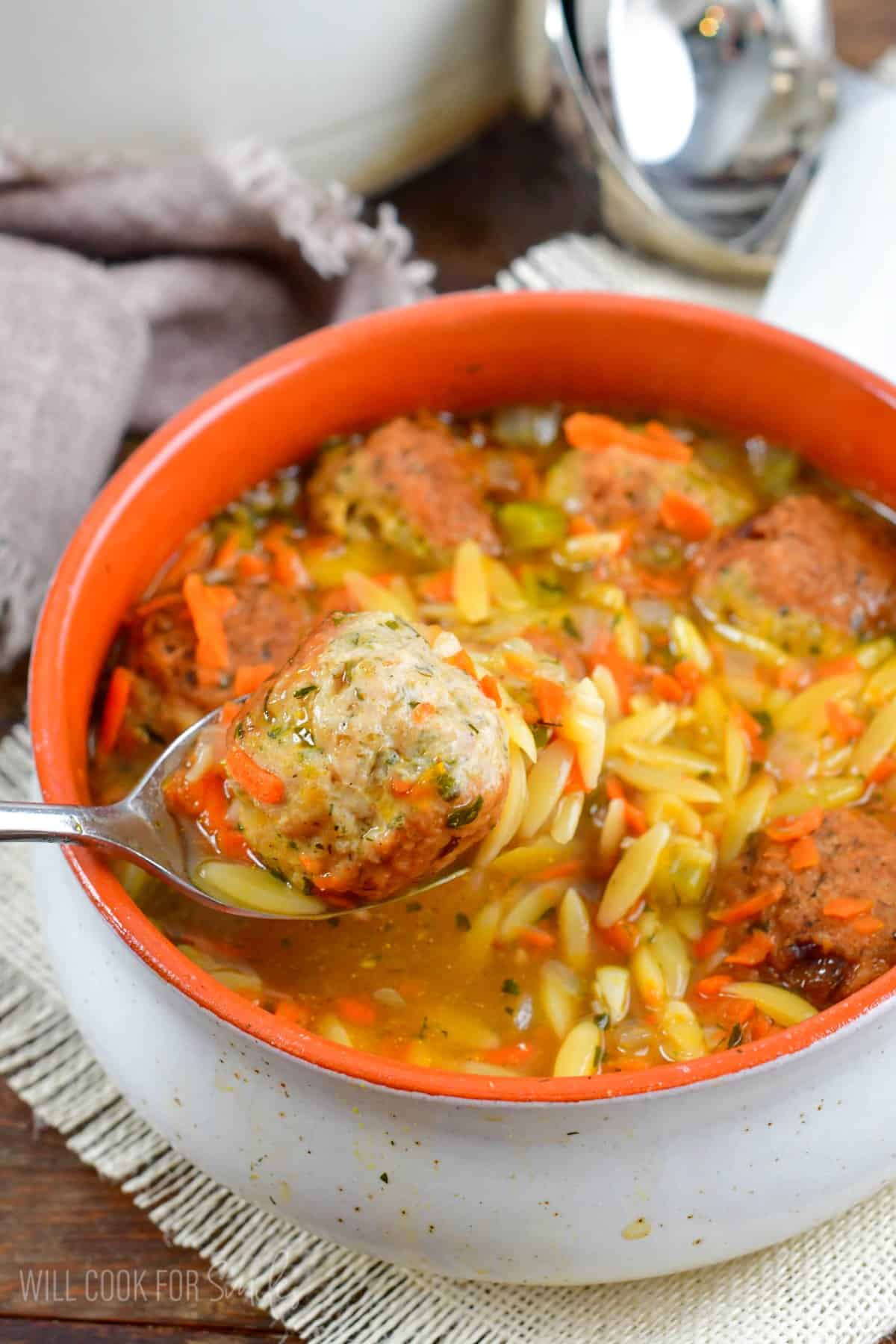 Spooning out a meatball from a bowl of chicken meatball orzo soup.