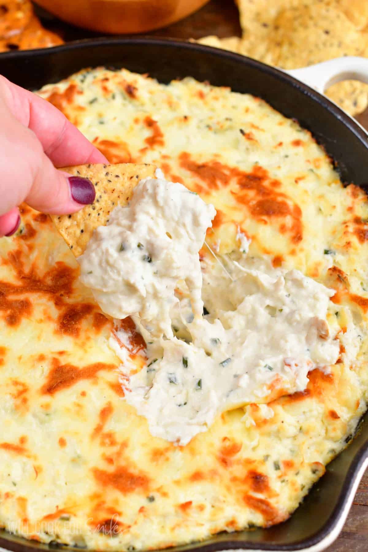 scooping out some creamy chicken dip from the skillet with a tortilla chip.