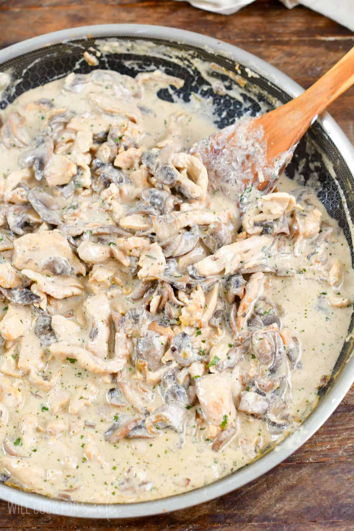 Cooked chicken stroganoff in a pan with a wooden spatula.