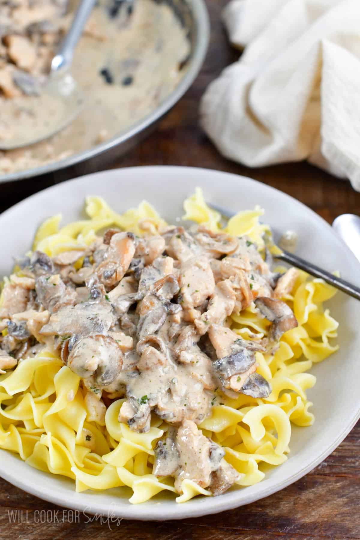 Chicken stroganoff over egg noodles in a bowl with a fork to the right.