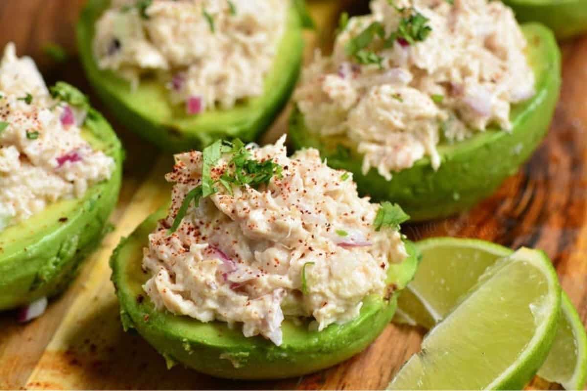 stuffed avocado halves topped with chicken salad and some parsley and lime wedges to the side.