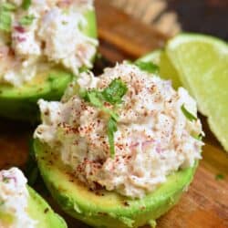 avocado half stuffed with chicken salad and topped with parsley and a lime wedge next to it.