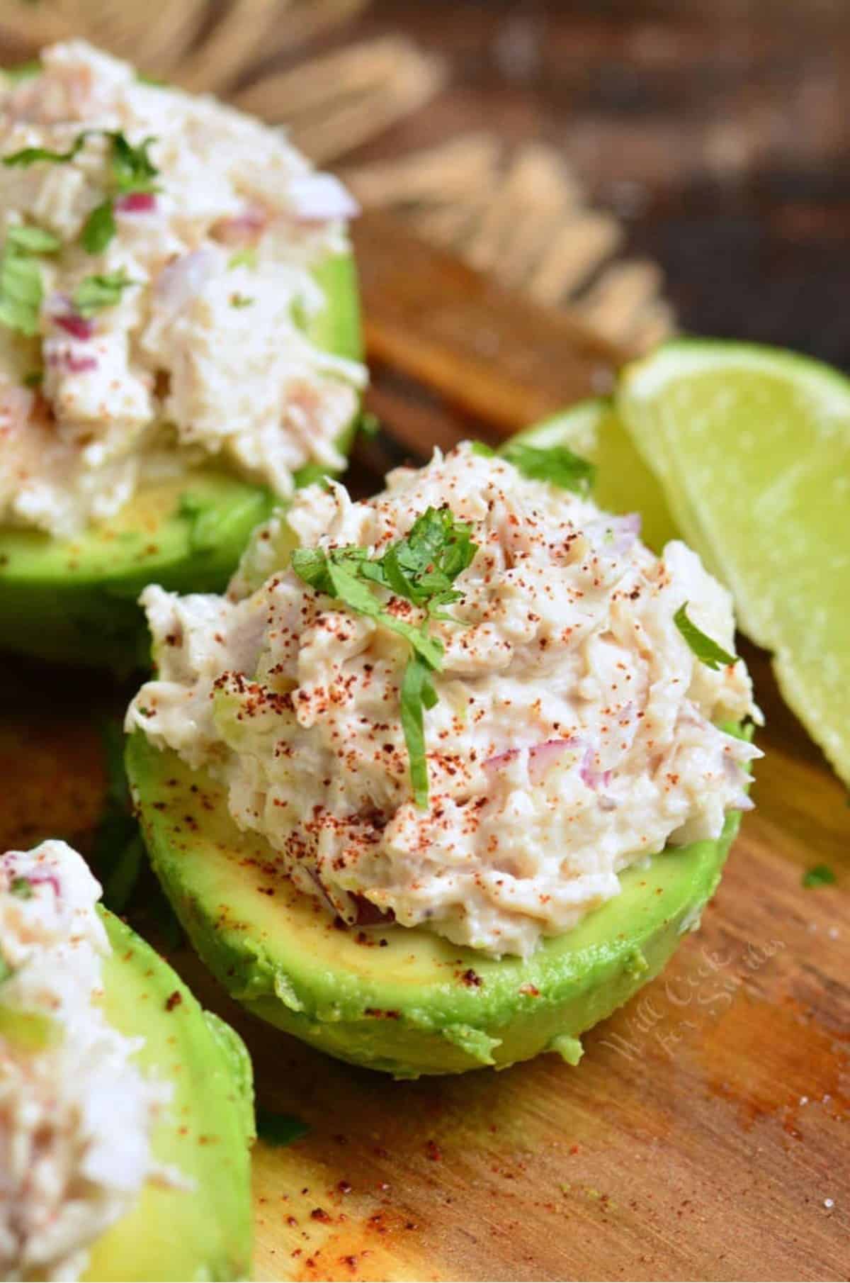 avocado half stuffed with chicken salad and topped with parsley and a lime wedge next to it.