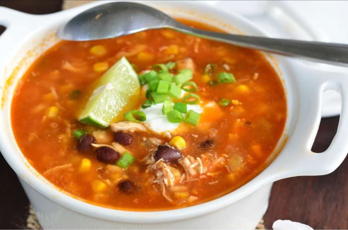 chicken tortilla soup in a bowl with a spoon topped with lime wedge, sour cream and green onion.