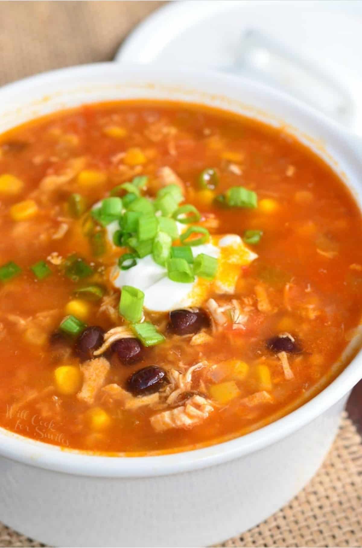 white bowl filled with chicken tortilla soup topped with green onion and sour cream.