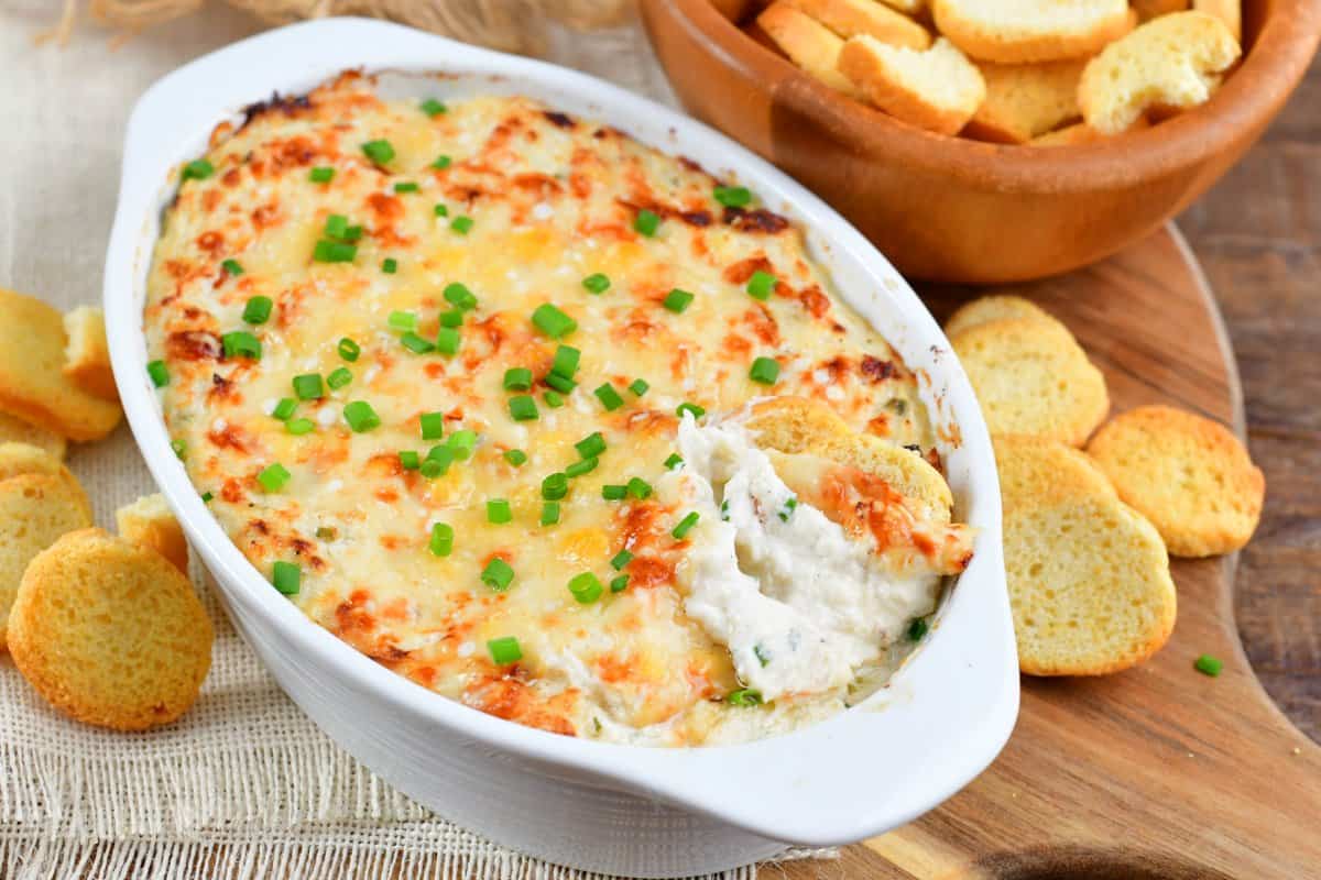hot baked crab dip in a white oval dish with some crackers in it and spread around it.