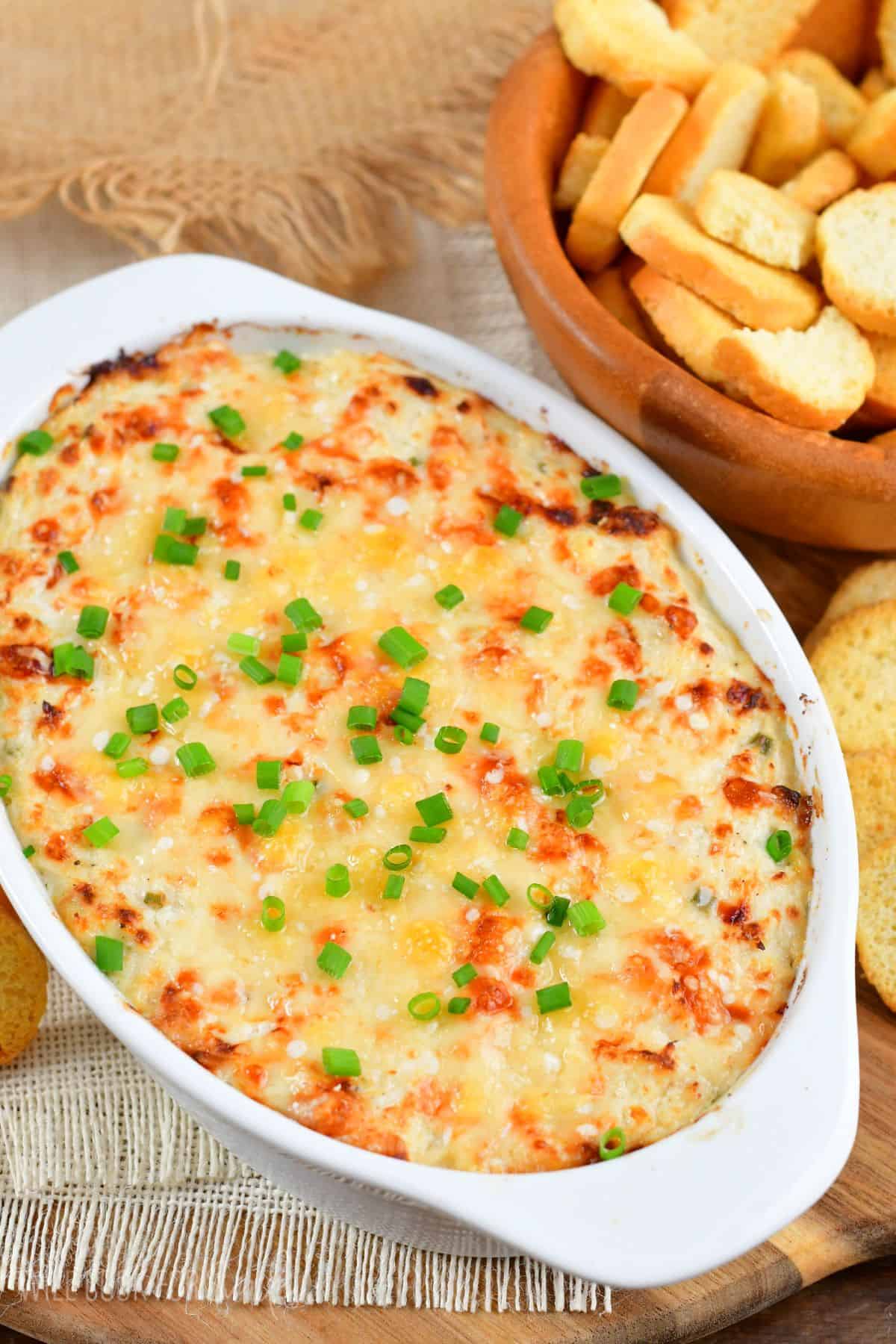 baked crab dip in a white dish with green onion and crackers in a bowl.