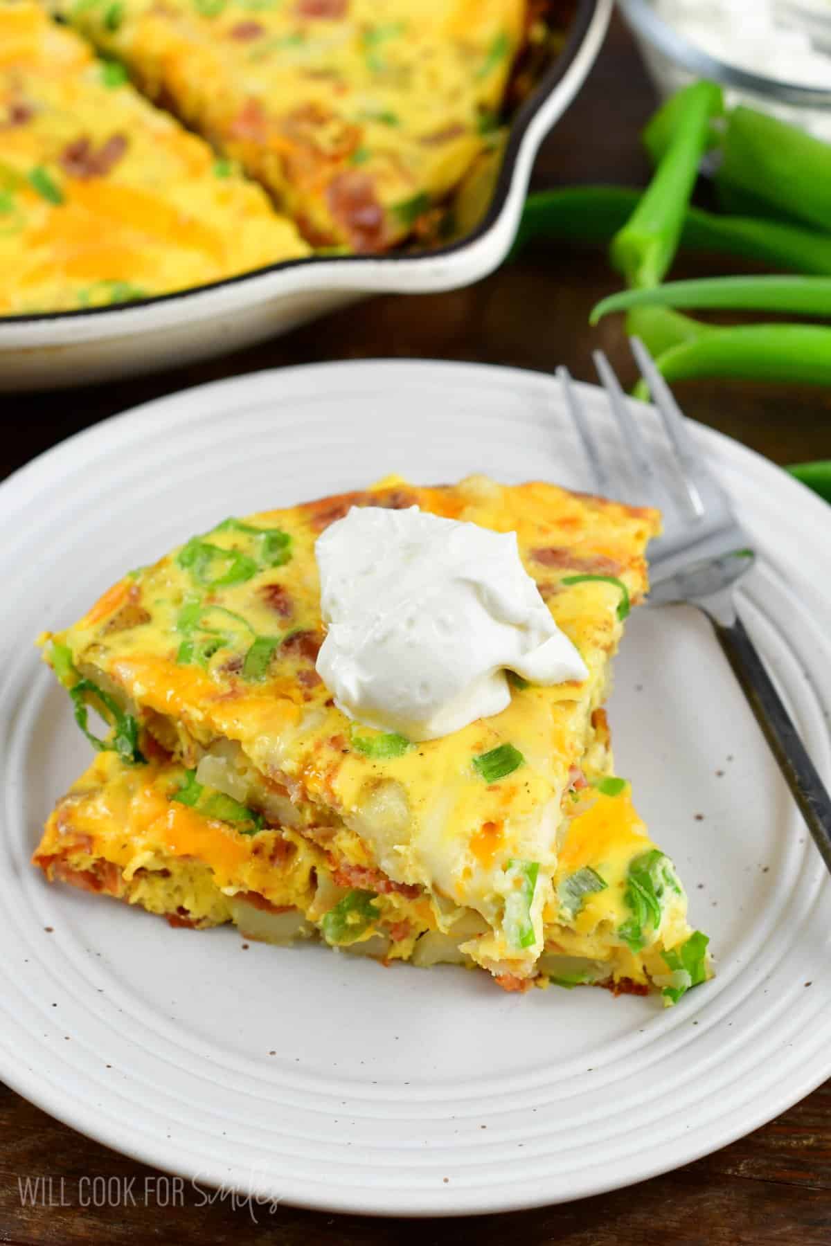 two breakfast bake triangles stacked on the plate with some sour cream on top.