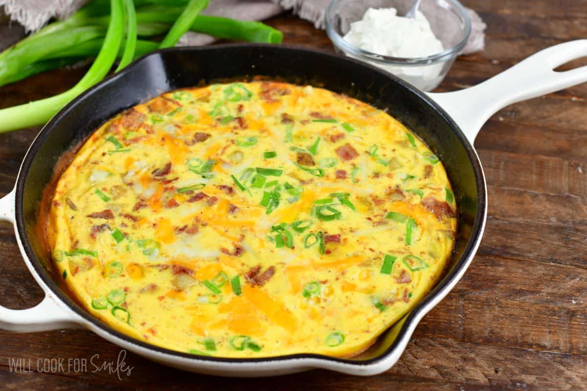 a skillet with breakfast bake of potatoes, bacon, green onion and cheese.