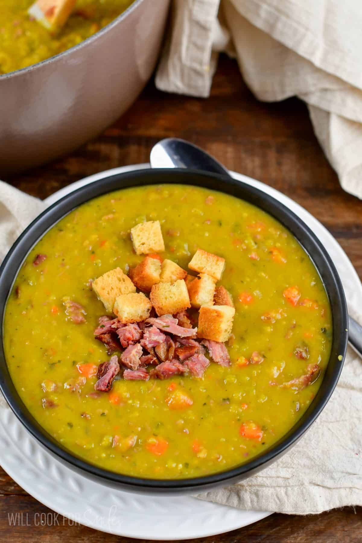 spilt pea soup in a bowl with croutons and ham on top.