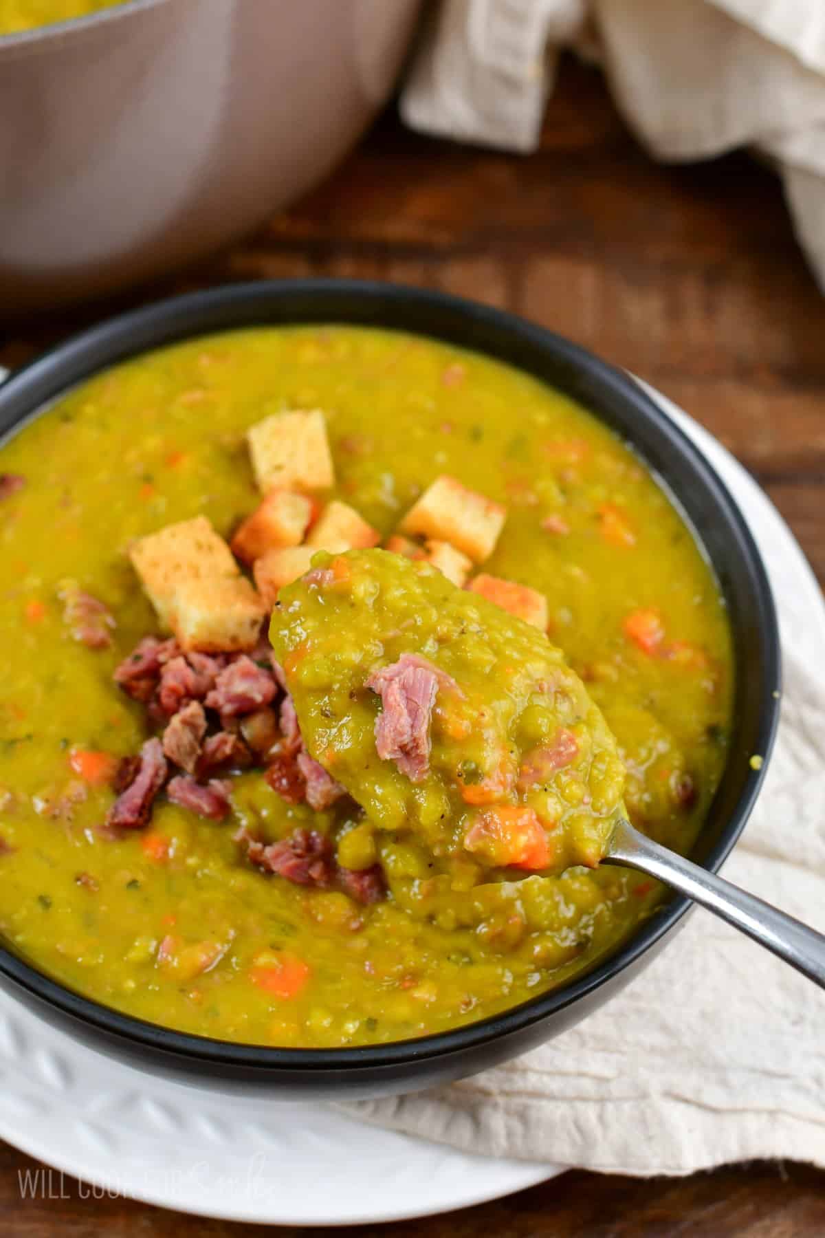 split pea soup in a bowl with ham and croutons on top and a spoon scooping some out.