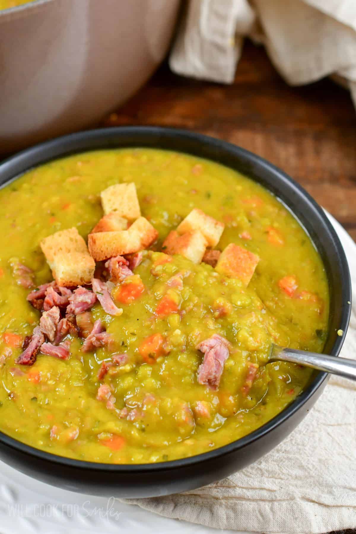 split pea soup in a bowl topped with croutons and ham with a spoon.