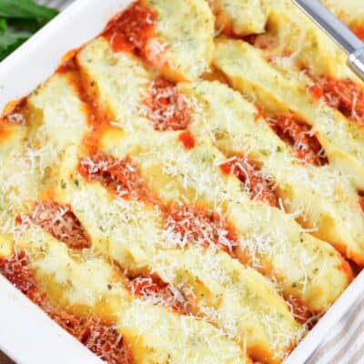 three rows of baked stuffed shells in marinara sauce in a white baking dish.