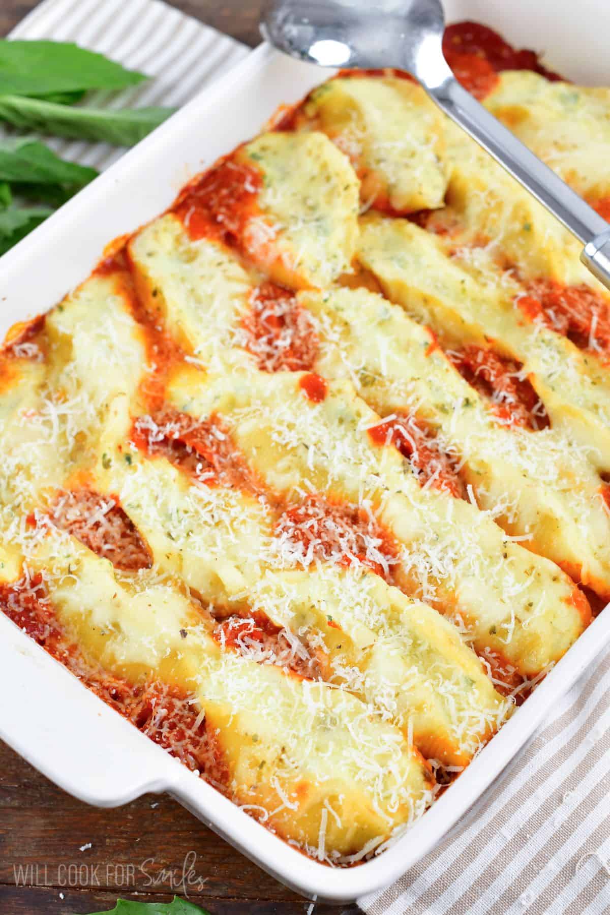 three rows of baked stuffed shells in marinara sauce in a white baking dish.