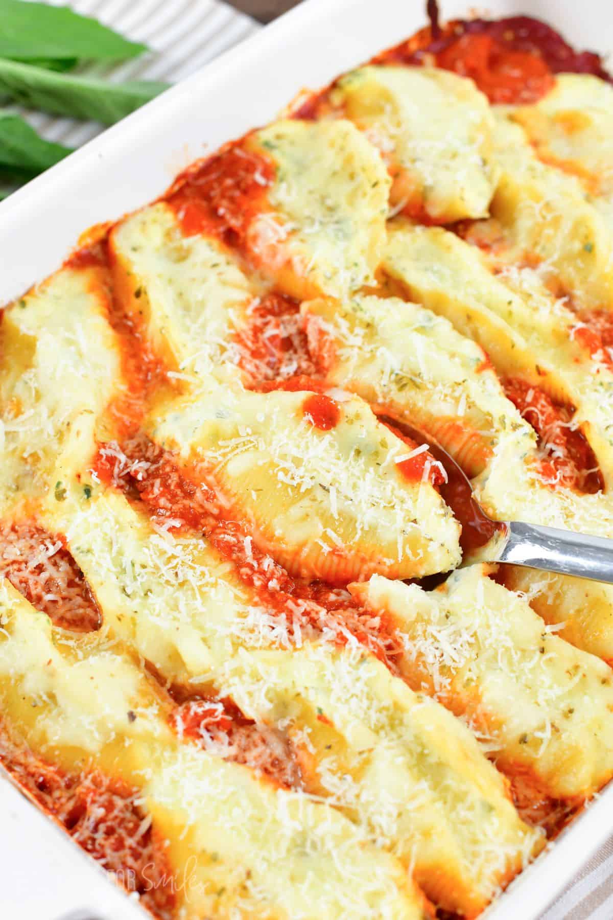 Scooping out one of the baked stuffed shells from the baking dish with a silver spoon.