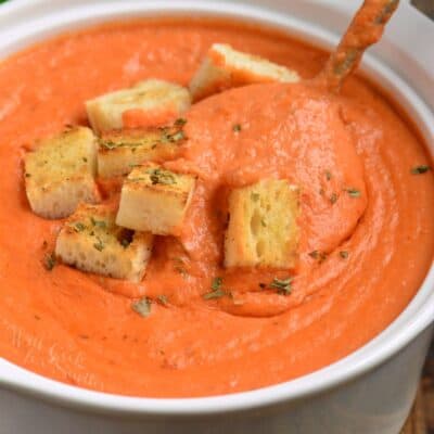 tomato bisque in a bowl with croutons on top and a spoon scooping some up.