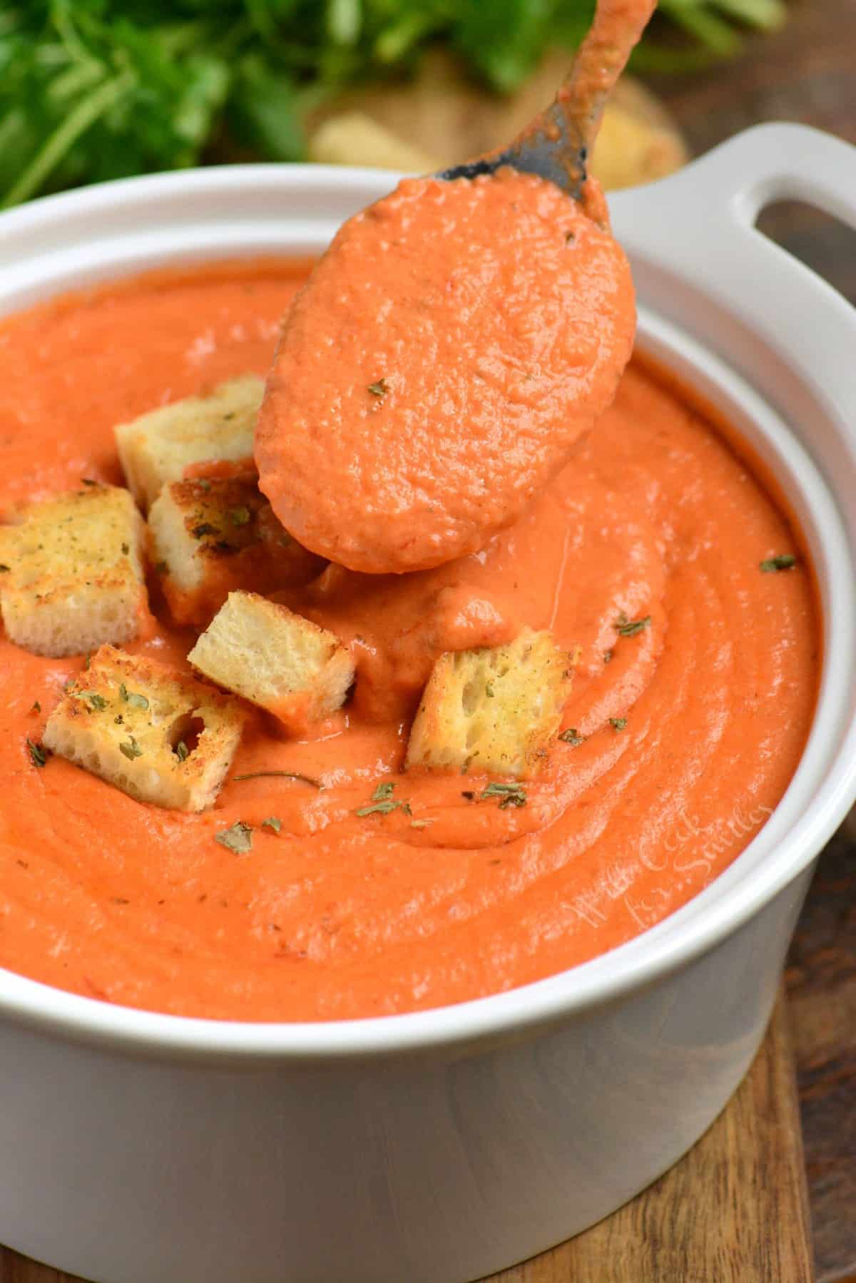 tomato soup in a bowl with croutons on top and a spoon scooping some of the soup.