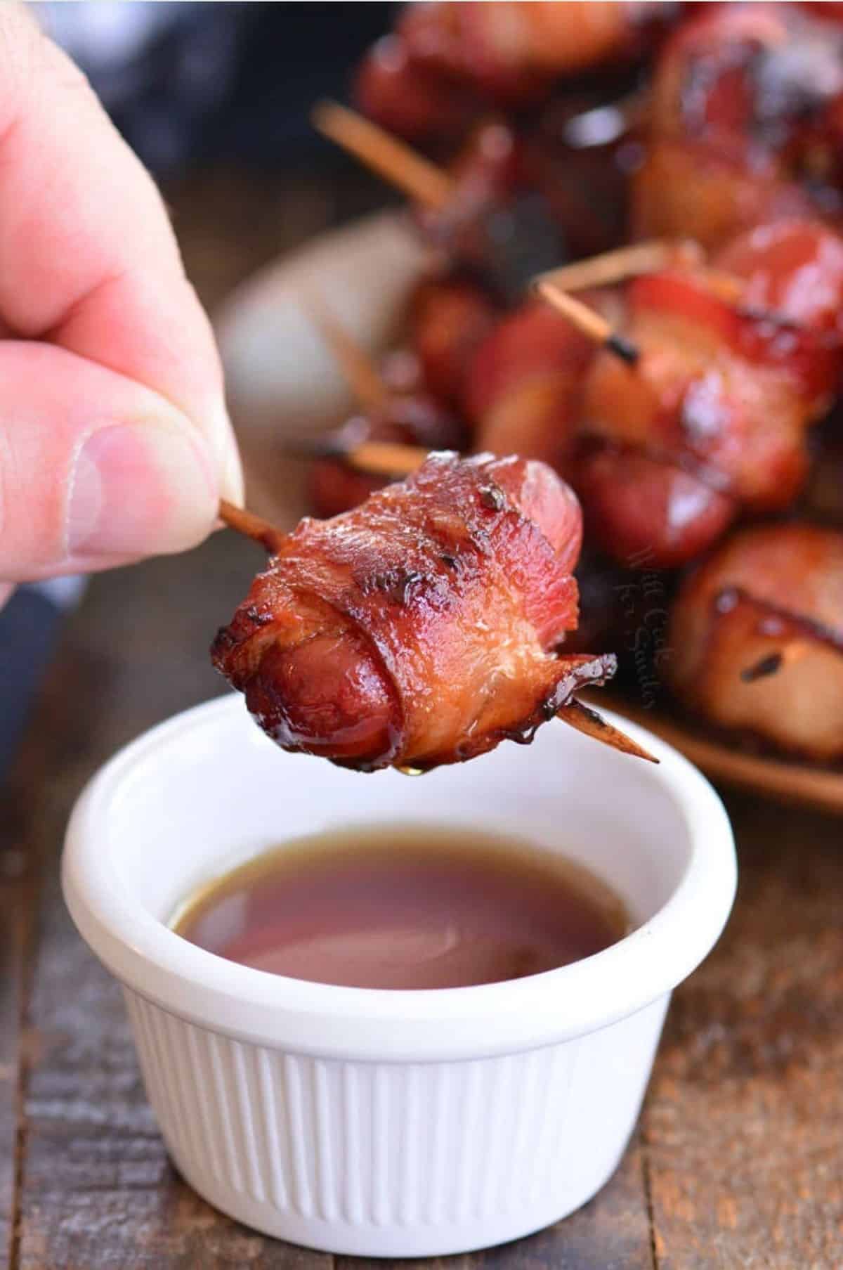 dipping a bacon wrapped little smokies into some maple syrup.