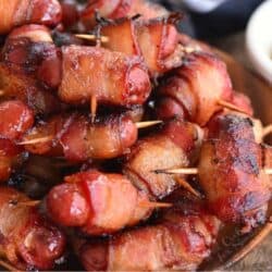 several crispy baked bacon wrapped little sausages stacked on the plate.