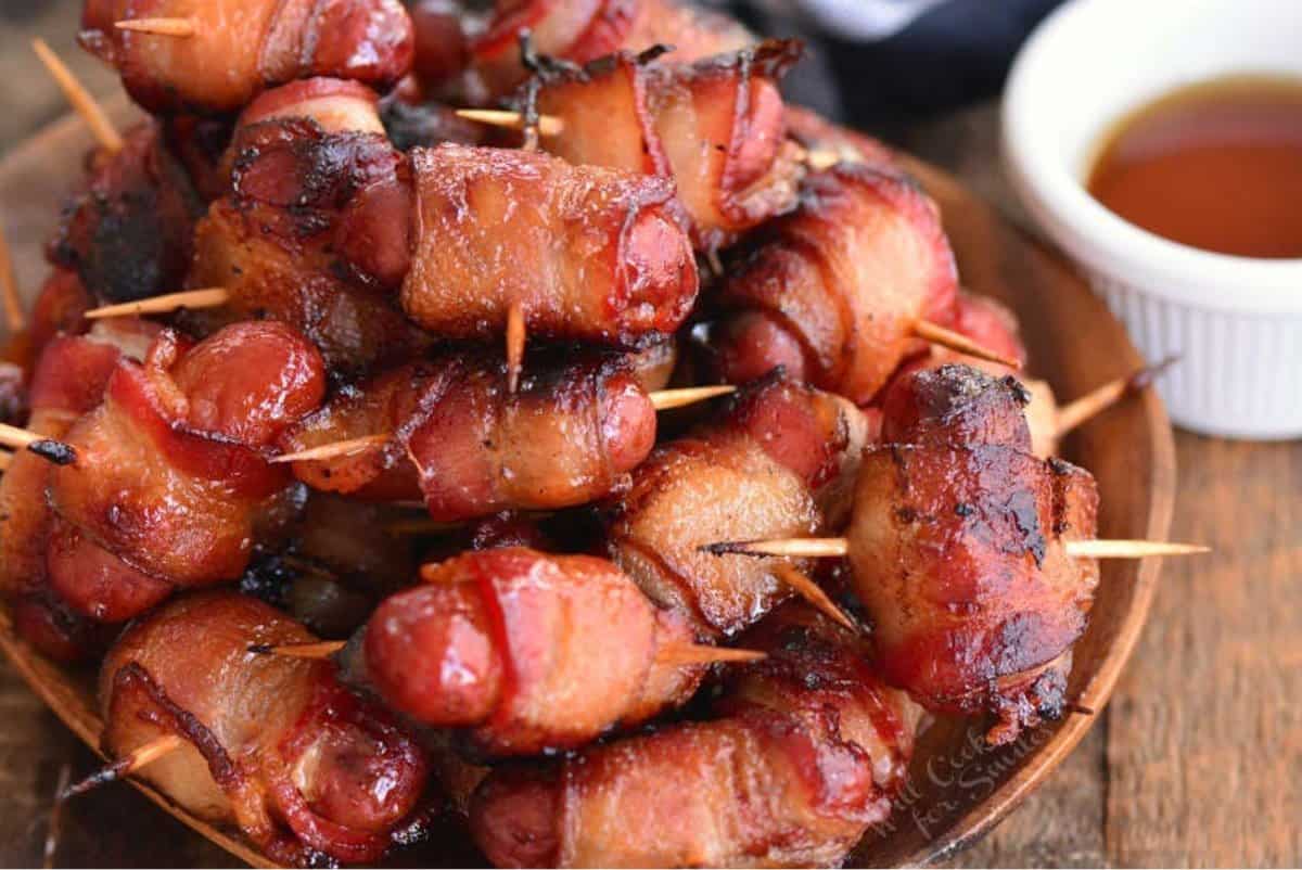 several crispy baked bacon wrapped little sausages stacked on the plate.