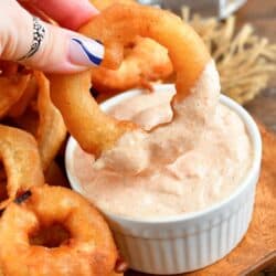 Beer battered onion ring being dopped into sauce that is in a small bowl.