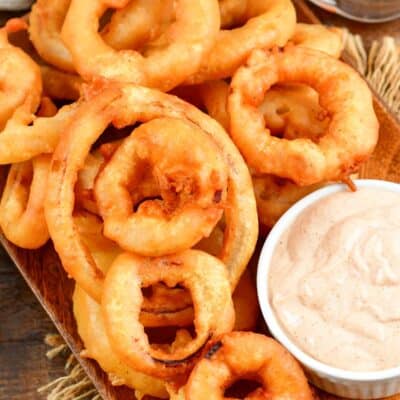 Beer Battered onion rings on a plate with dipping sauce in a a small bowl.