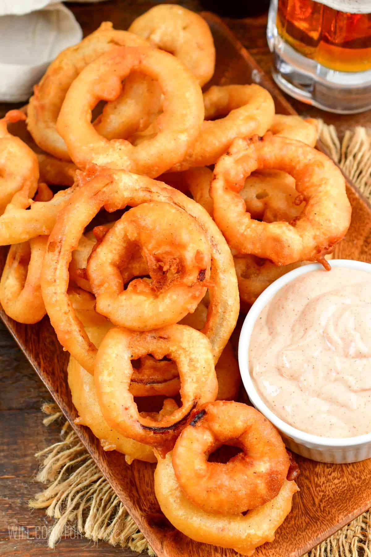 Beer Battered onion rings on a plate with dipping sauce in a a small bowl.