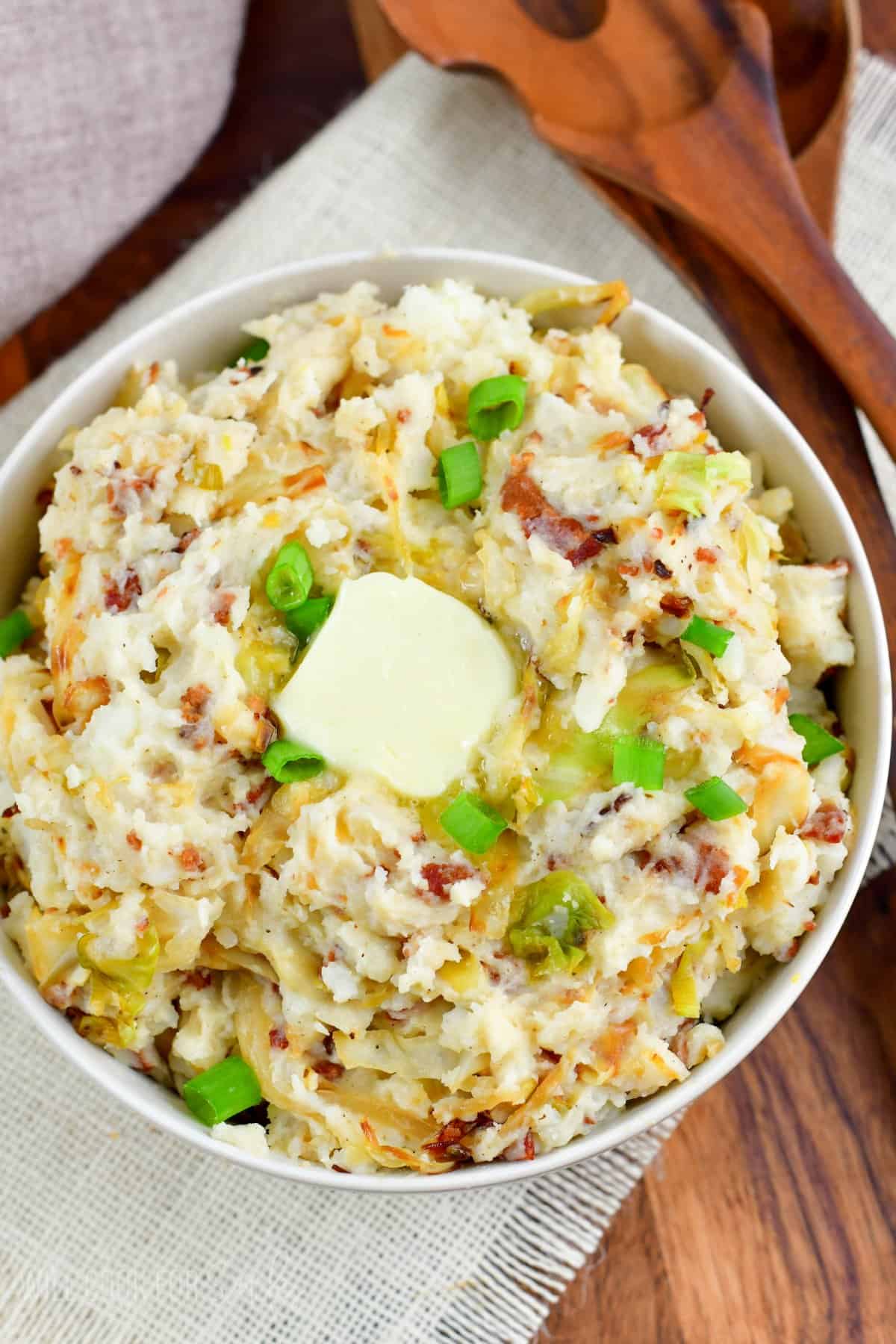 Colcanon irish mashed potatoes in a bowl with butter on top and green onions as garnish.