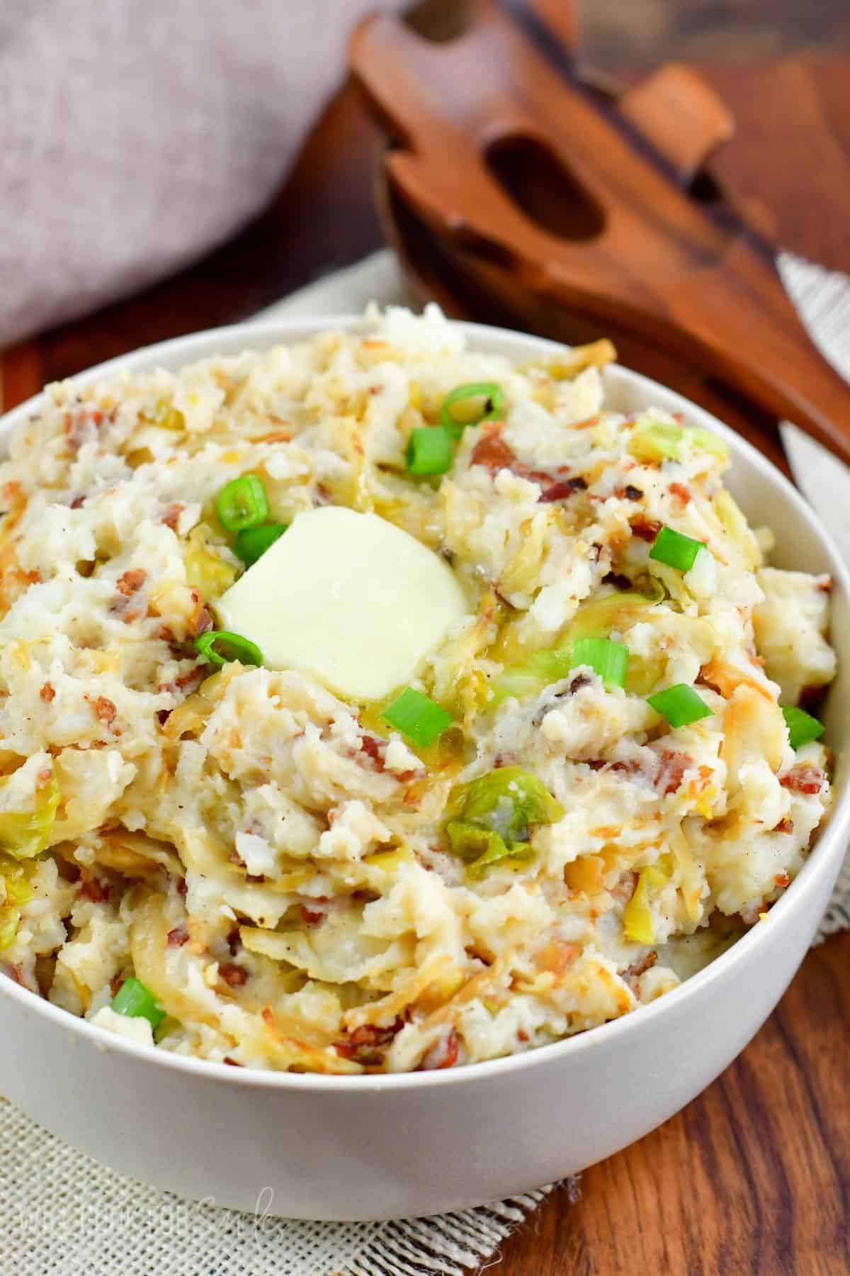 Colcannon in a bowl with butter and green onions as garnish.