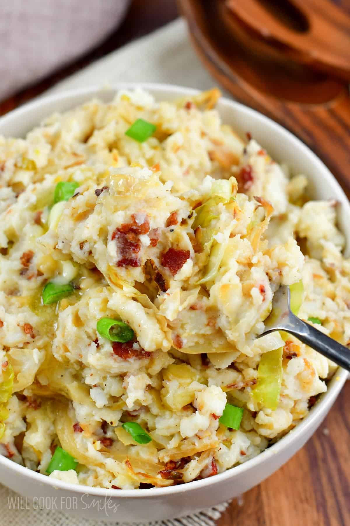 Colcannon in a bowl and scooping some out of the bowl with a fork.