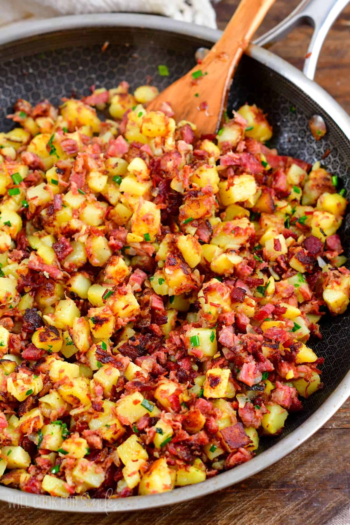 Cooked corn beef hash in a pan with a wooden spoon.