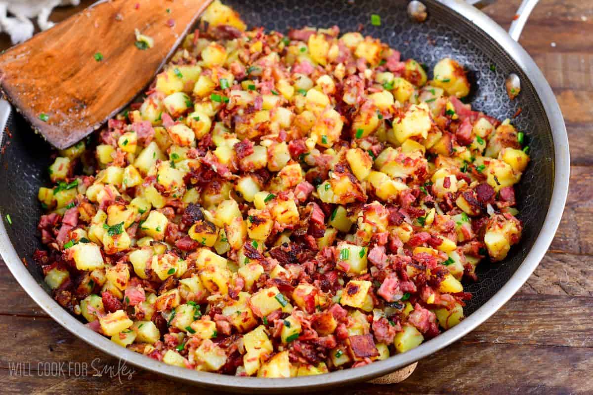 corned beef hash in a pan with a wooden spoon.