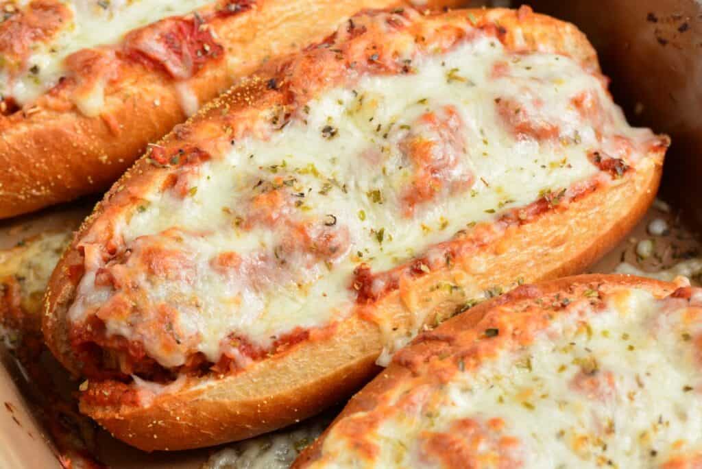 Close-up of cheesy garlic bread, topped with melted mozzarella and sprinkled with herbs. The bread has a golden-brown crust, and the cheese appears gooey and slightly browned. Multiple pieces are placed together, filling the frame with a savory, appetizing look.