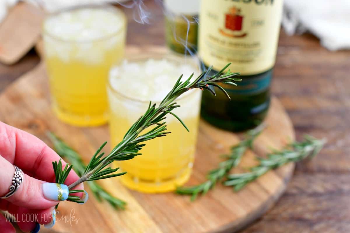 holding a sprig of rosemary with two irish lemonades in the background