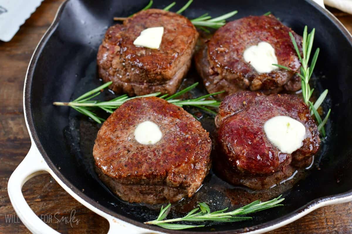 four filet mignon steaks with melting butter on top and rosemary next to them.