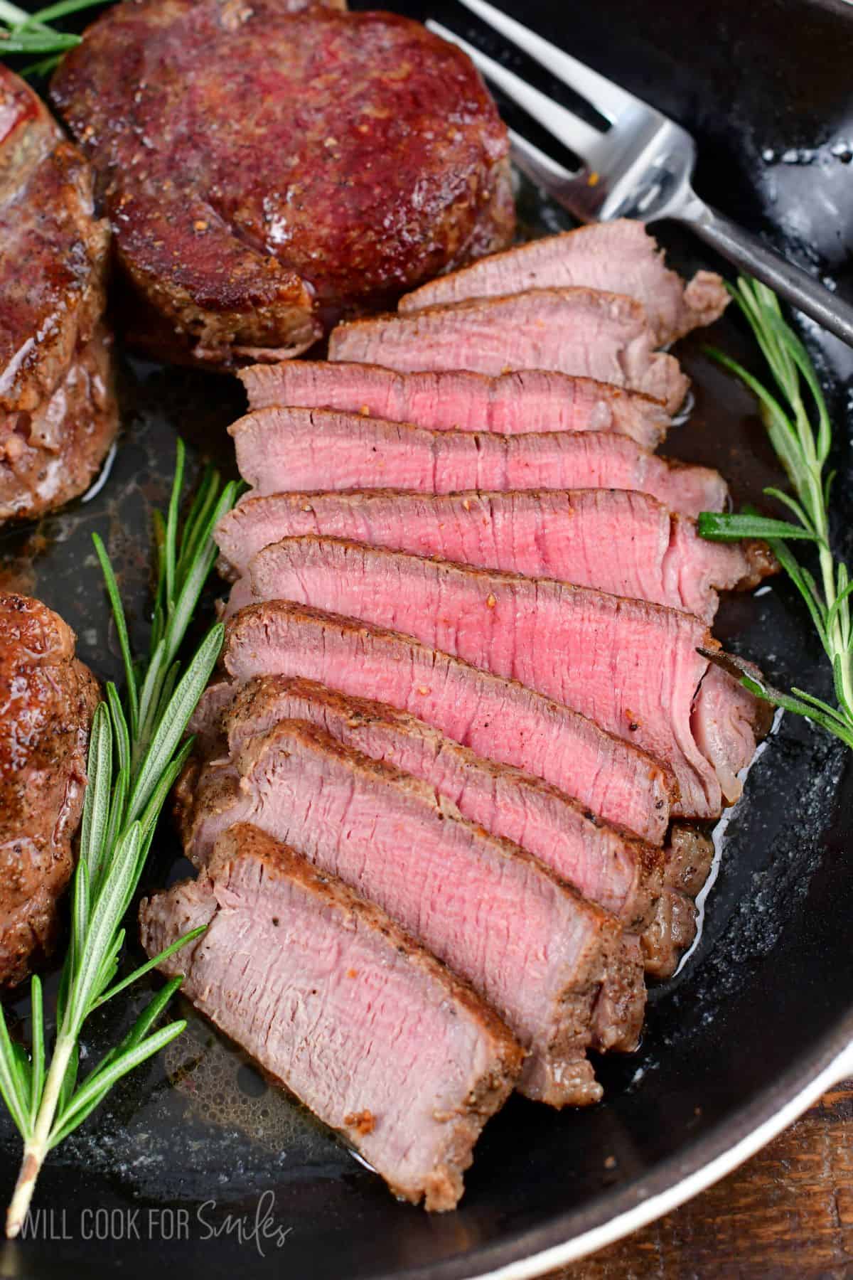 sliced filet mignon steak in a skillet with others not sliced next to it.