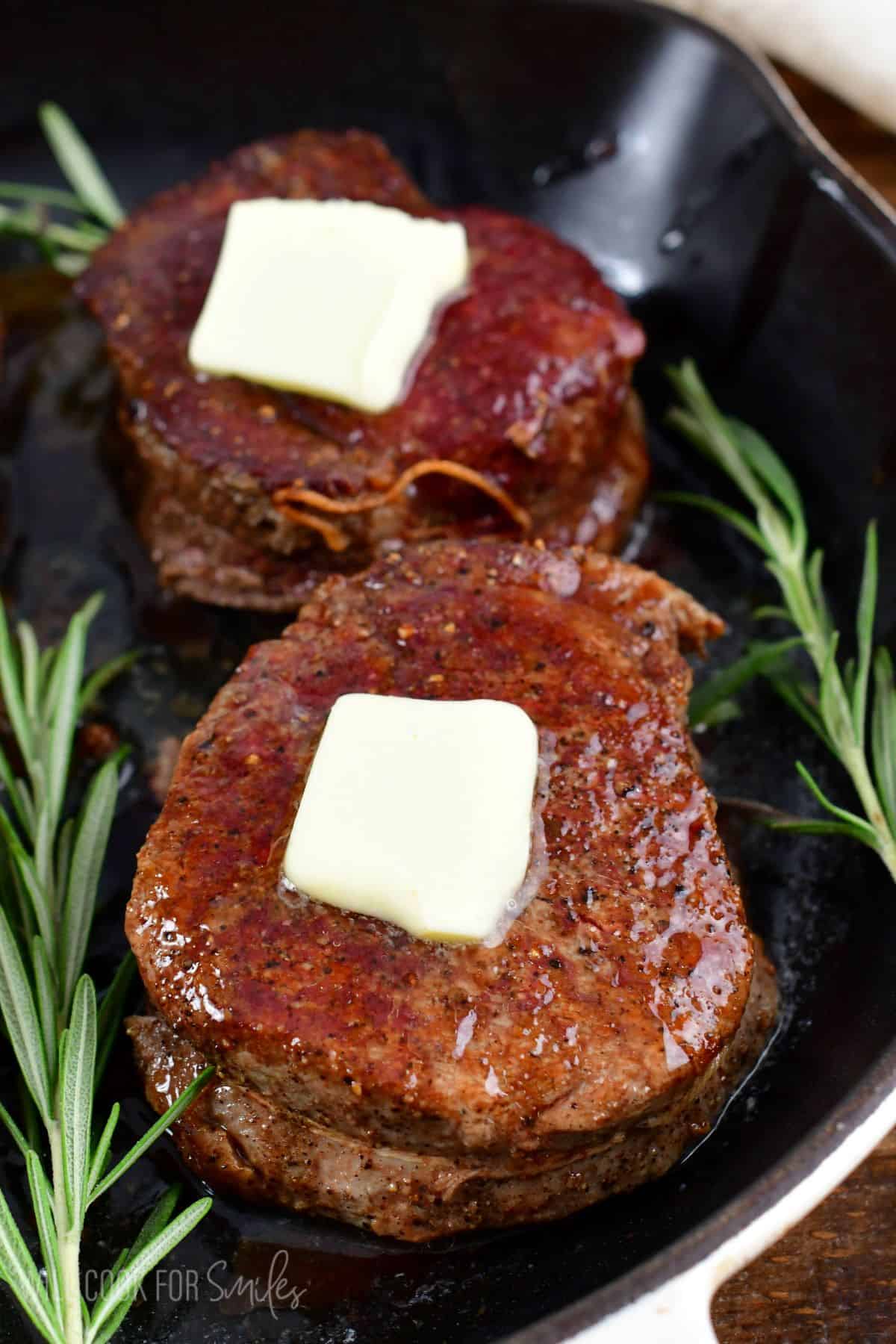 two gilet mignon steaks topped with butter and rosemary sprigs next to it.