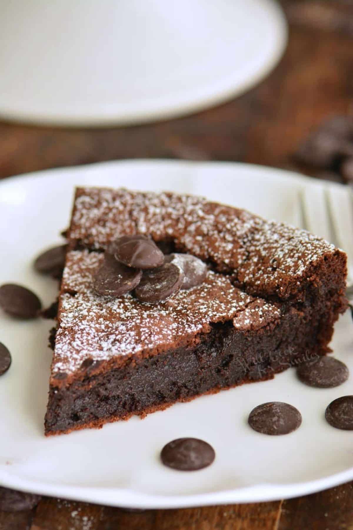 slice of flourless chocolate cake on the plate with some chocolate chips around.