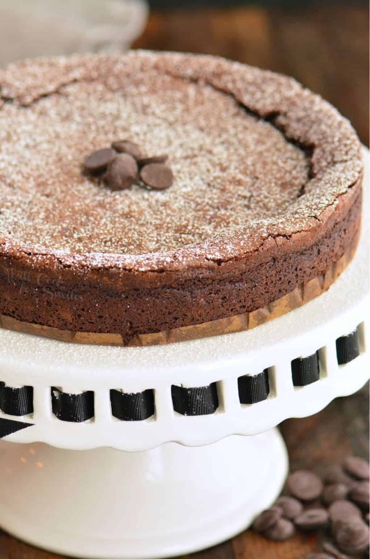 flourless chocolate cake topped with powdered sugar and chocolate chips on the cake stand.