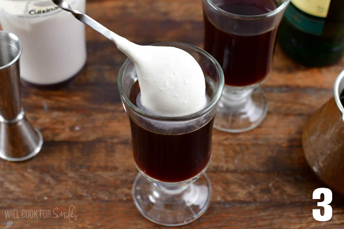 Adding some cream with a spoon to glasss of Irish coffee.