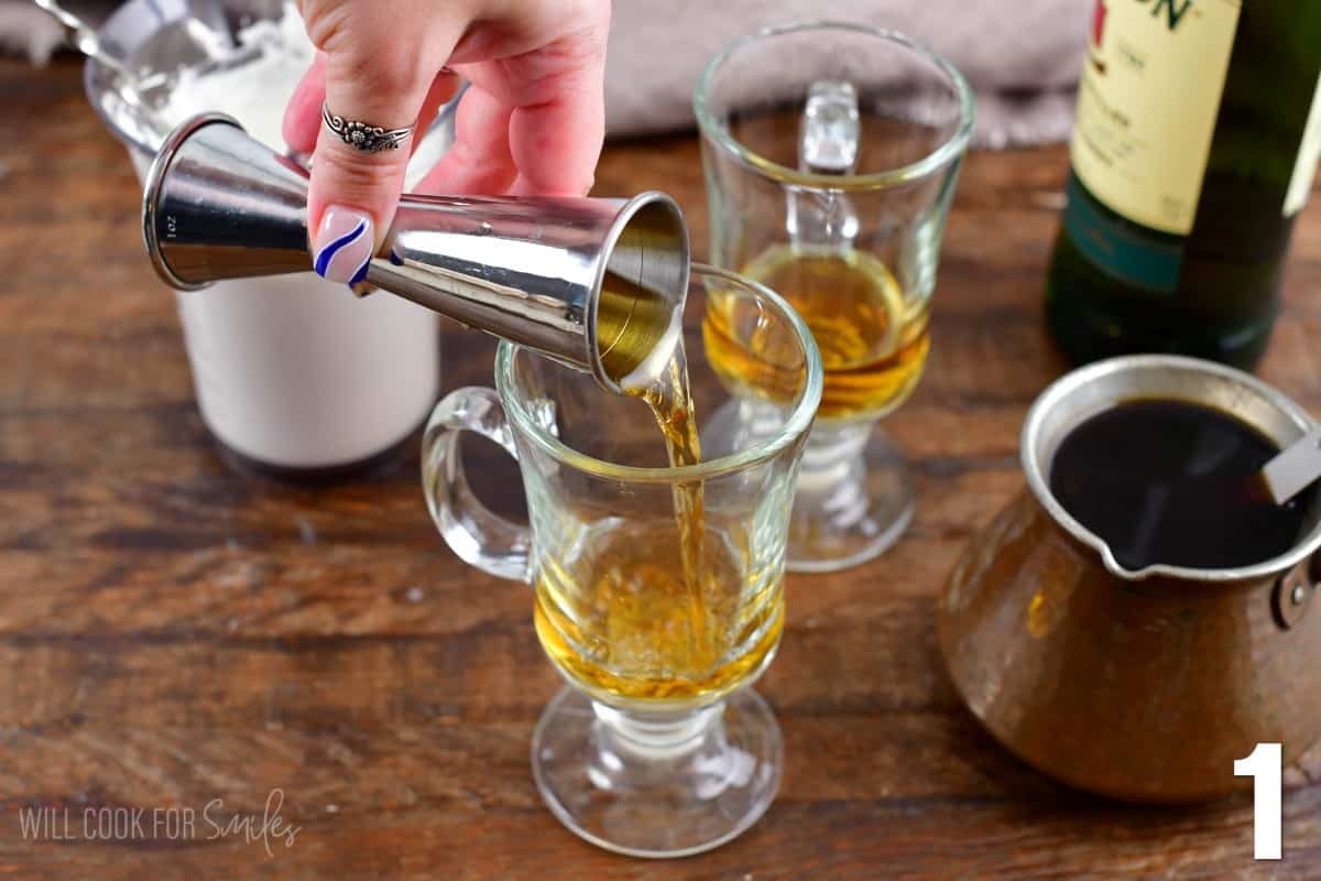 Adding whiskey into a glass for Irish coffee and a pot of coffee next to it.