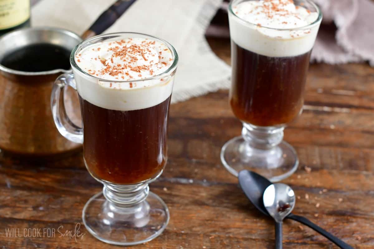 Irish coffe in a glass mug with cream on top on wood surface.