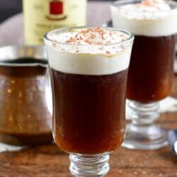 I glass filled with Irish coffee with another glass and a botle of Jameson in the background.