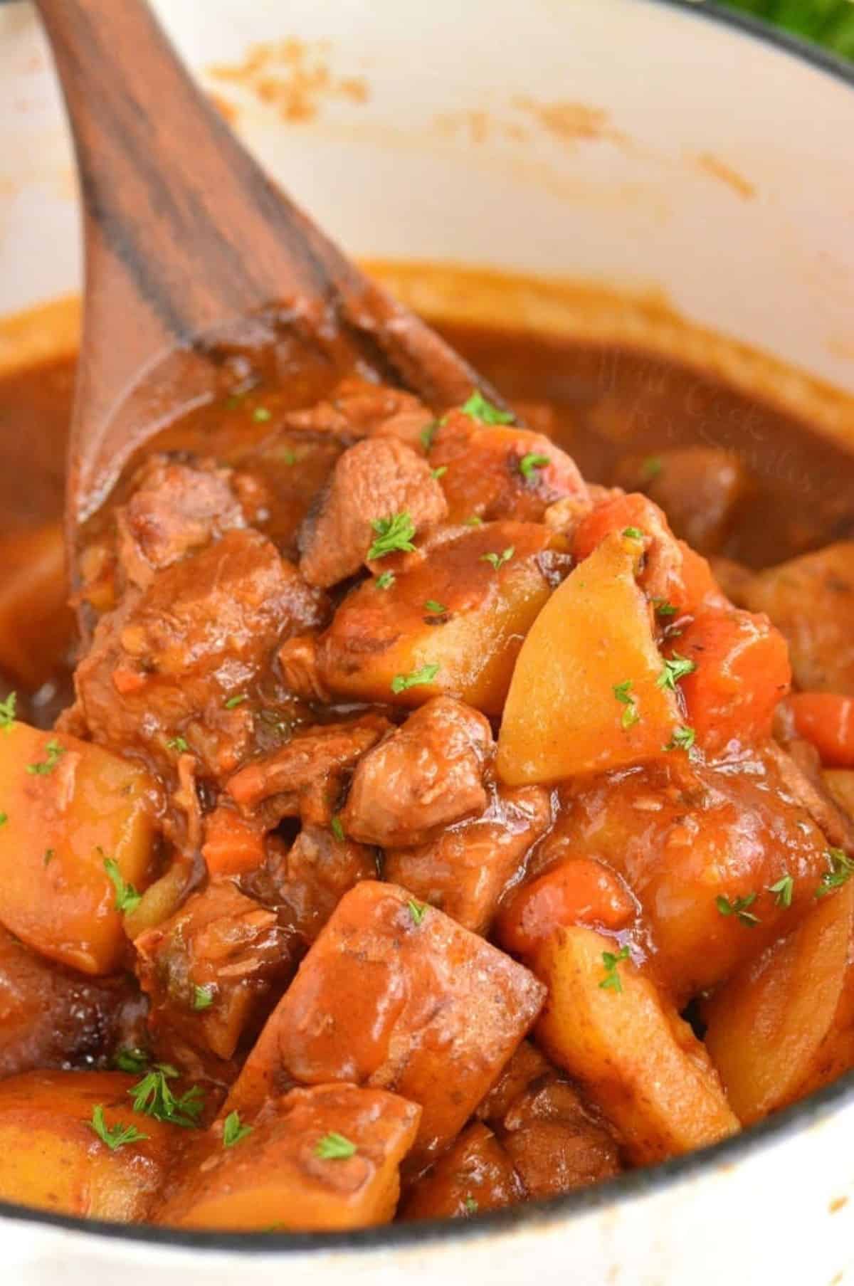 Scooping Irish beef stew from a pot with a wooden spoon.