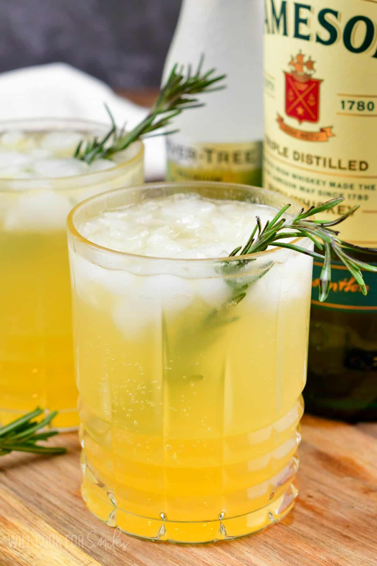 two glasses of Irish lemonade with rosemary as garnish on a wood surface.