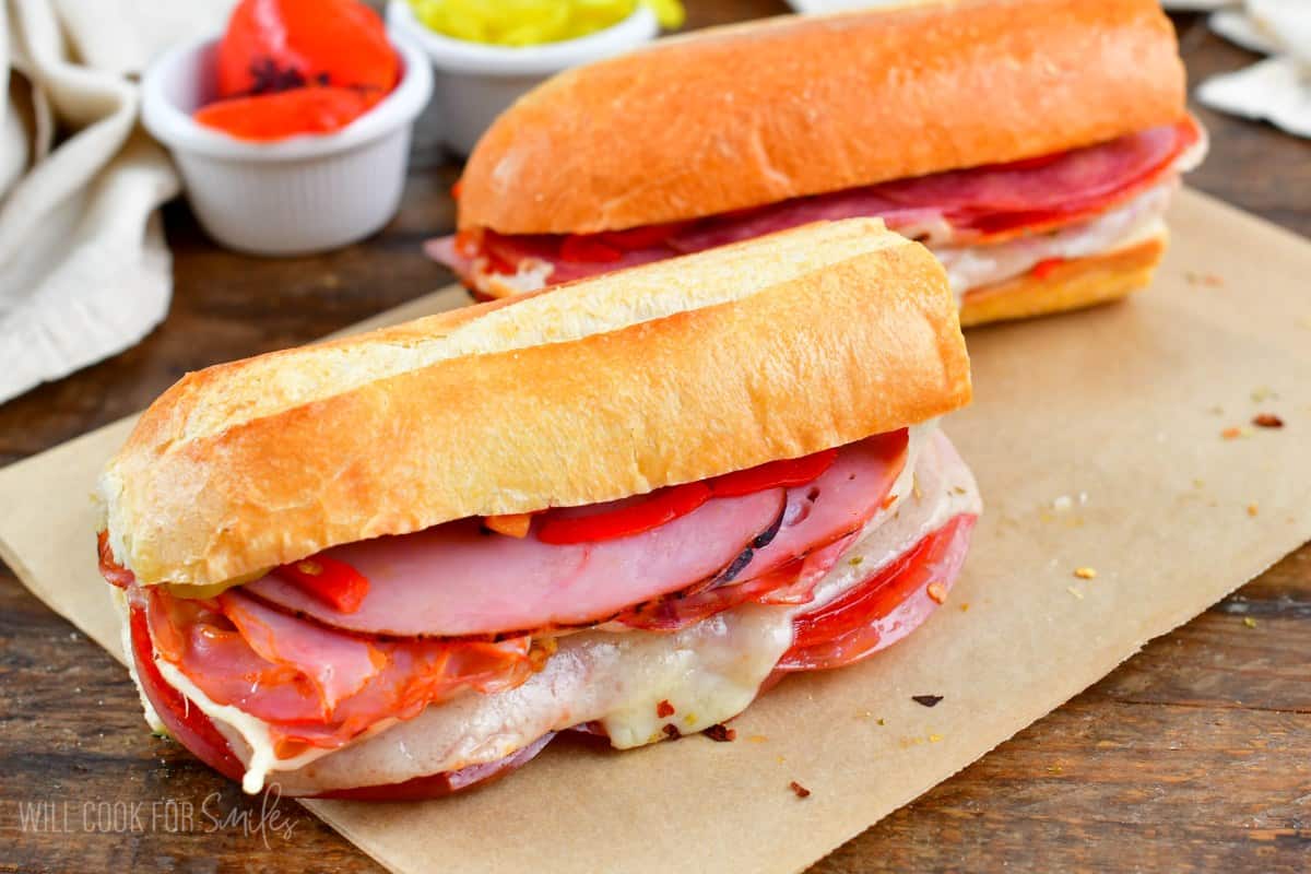 Two Italian subs on parchment paper on a wood surface.